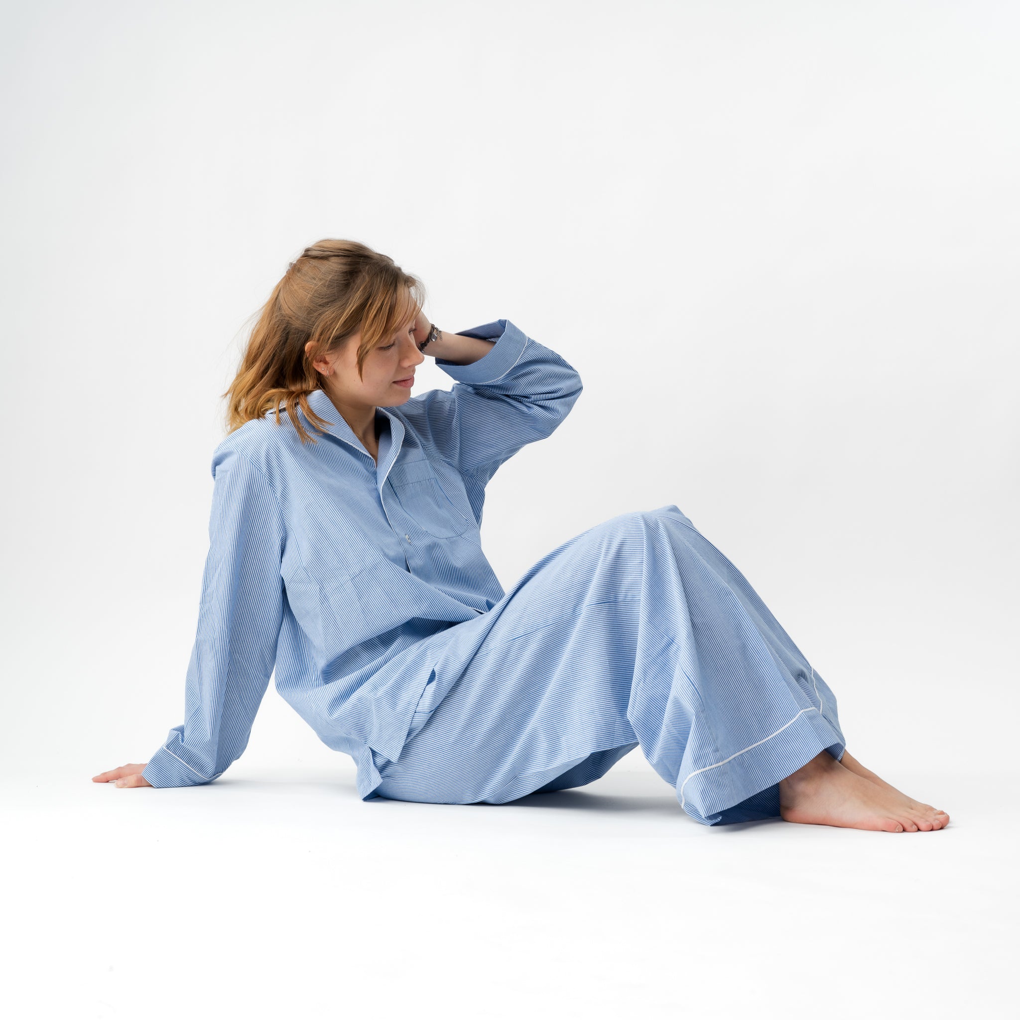Woman wearing a light blue pajama set sitting on a white background