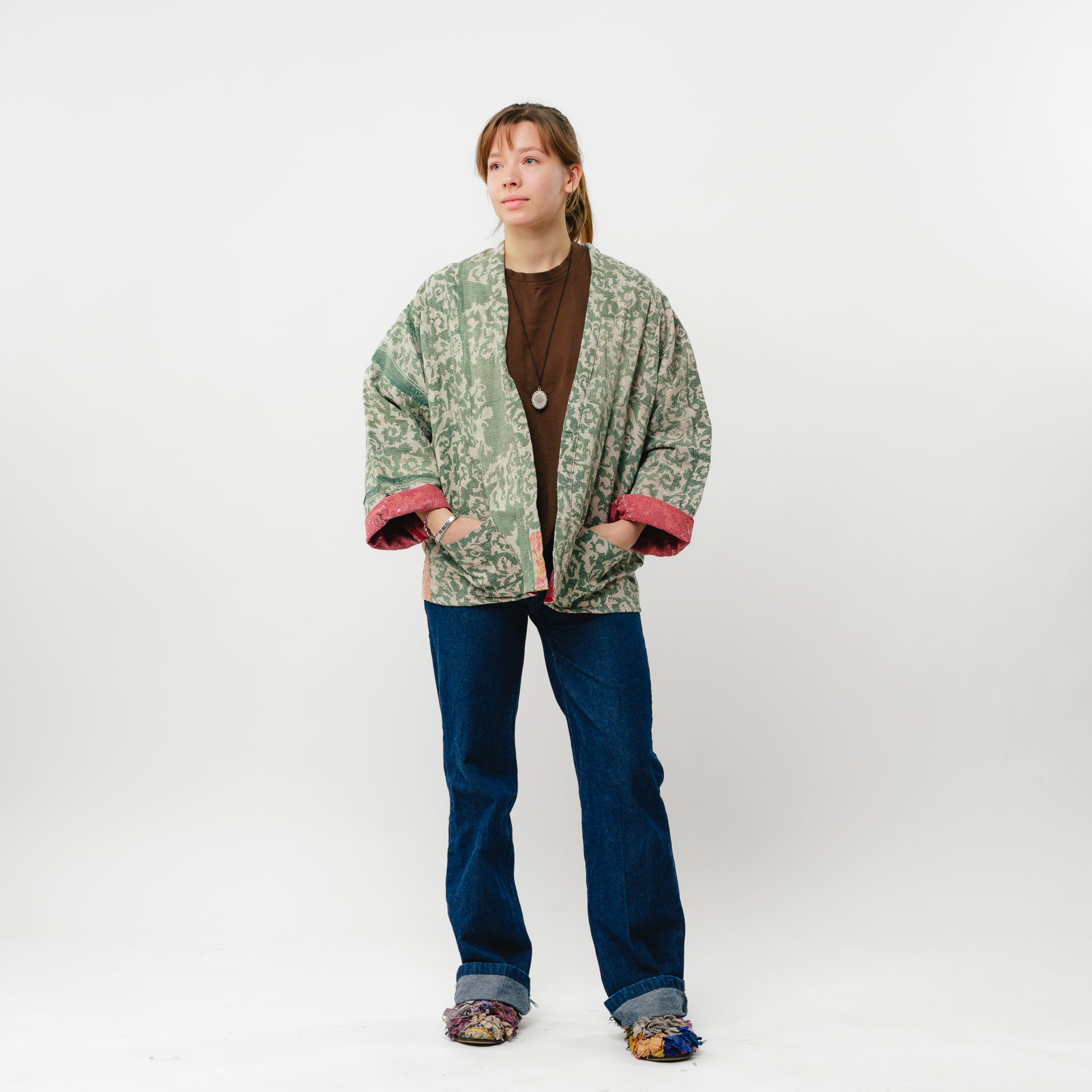 Person wearing a green patterned jacket and blue jeans on a white background