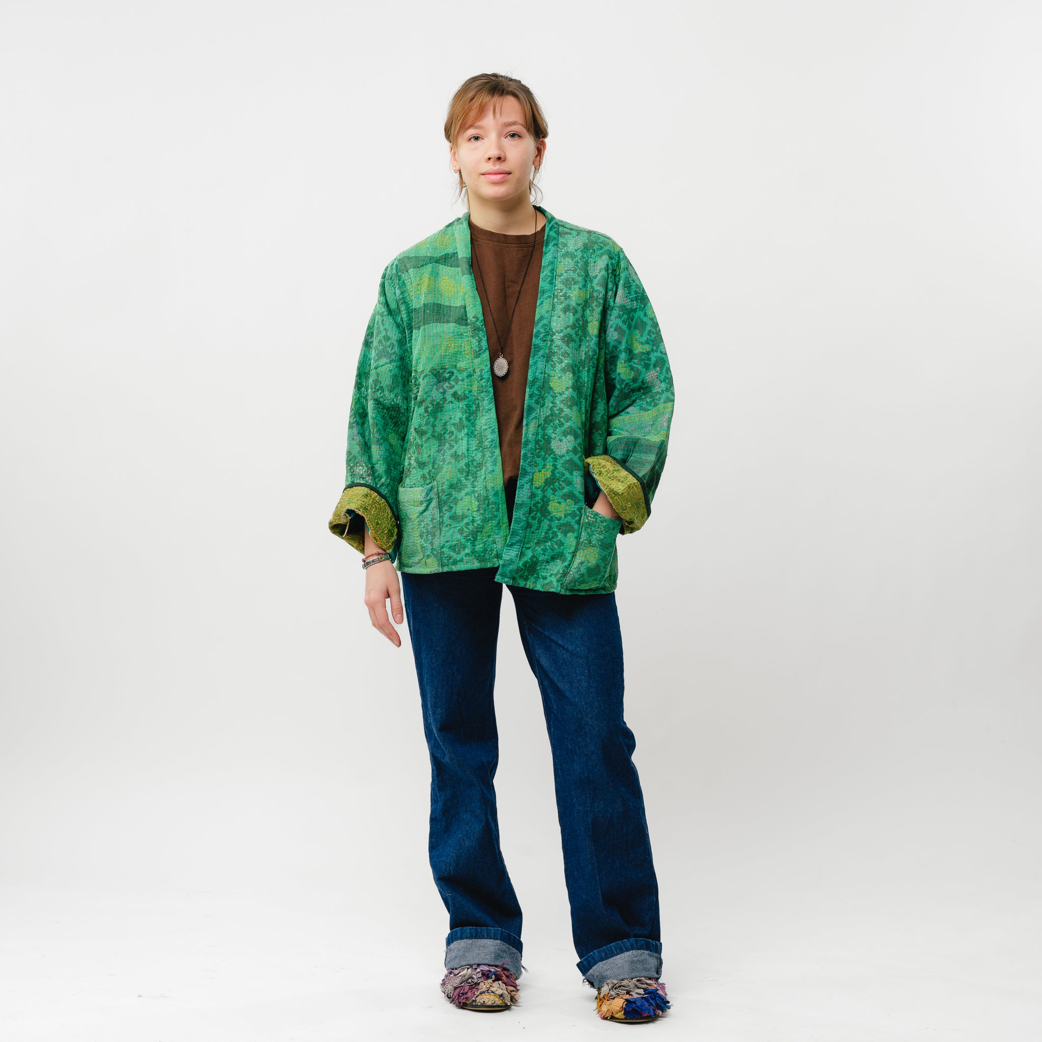 Person wearing a green patterned jacket and blue jeans on a white background