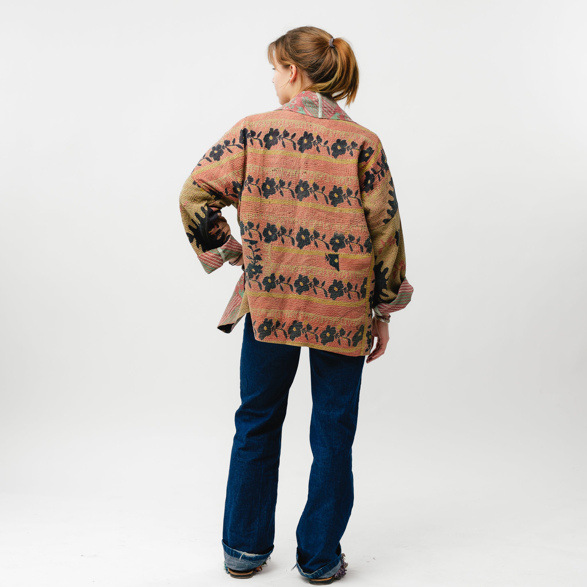 Person wearing a patterned shirt and blue jeans on a white background