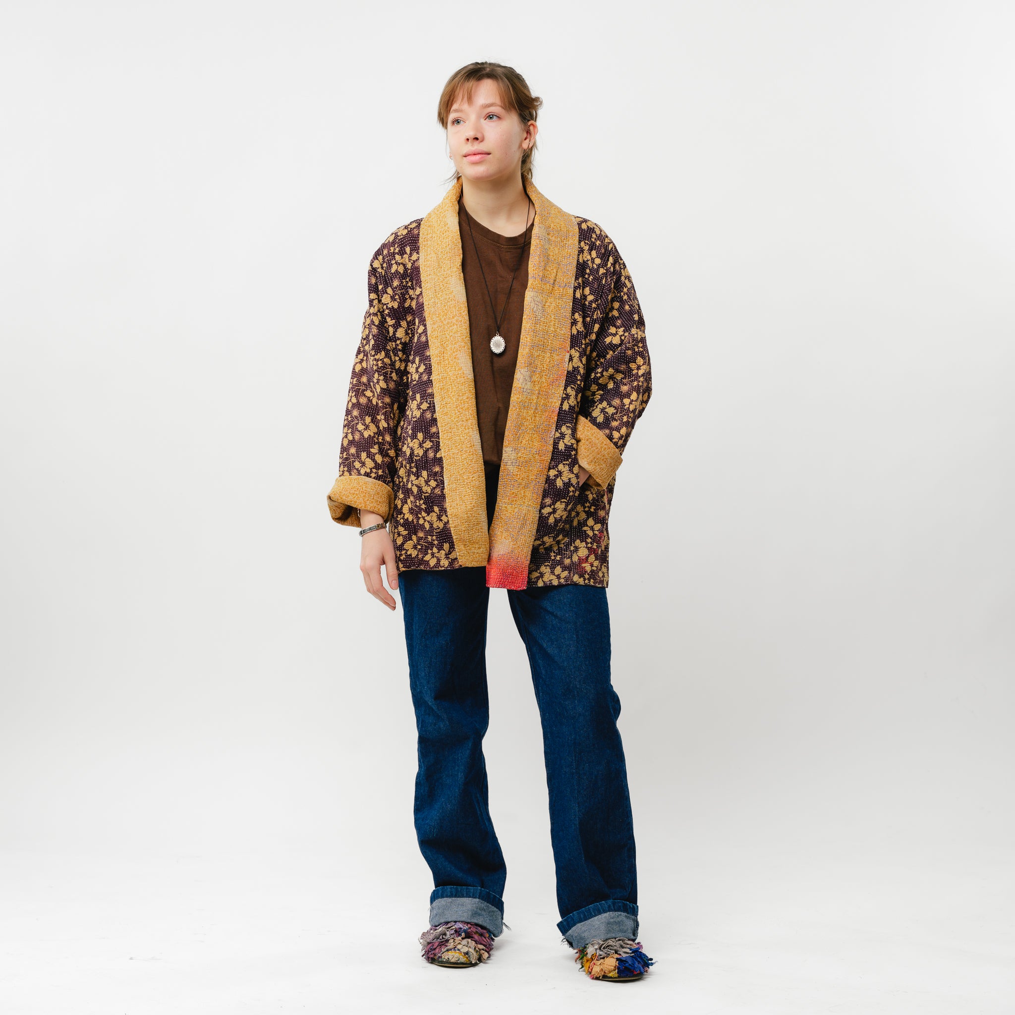 Person wearing a patterned jacket and jeans on a white background