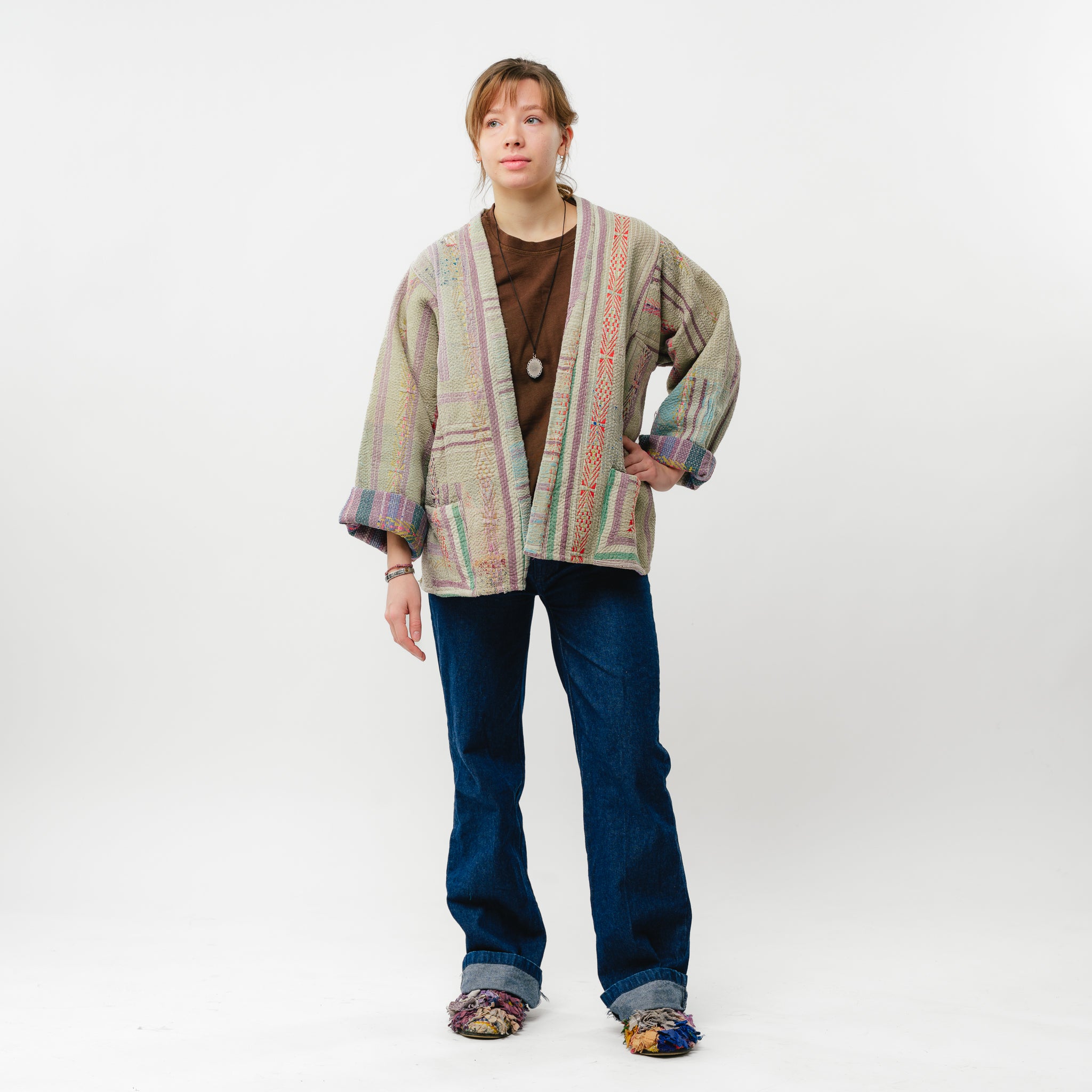 Person wearing a patterned cardigan and blue jeans on a white background
