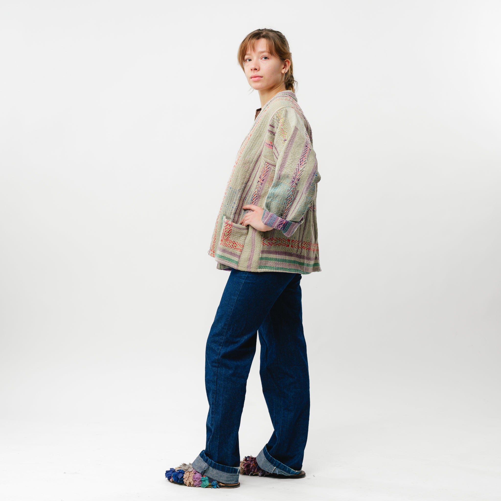 Person wearing a patterned jacket and blue pants on a white background