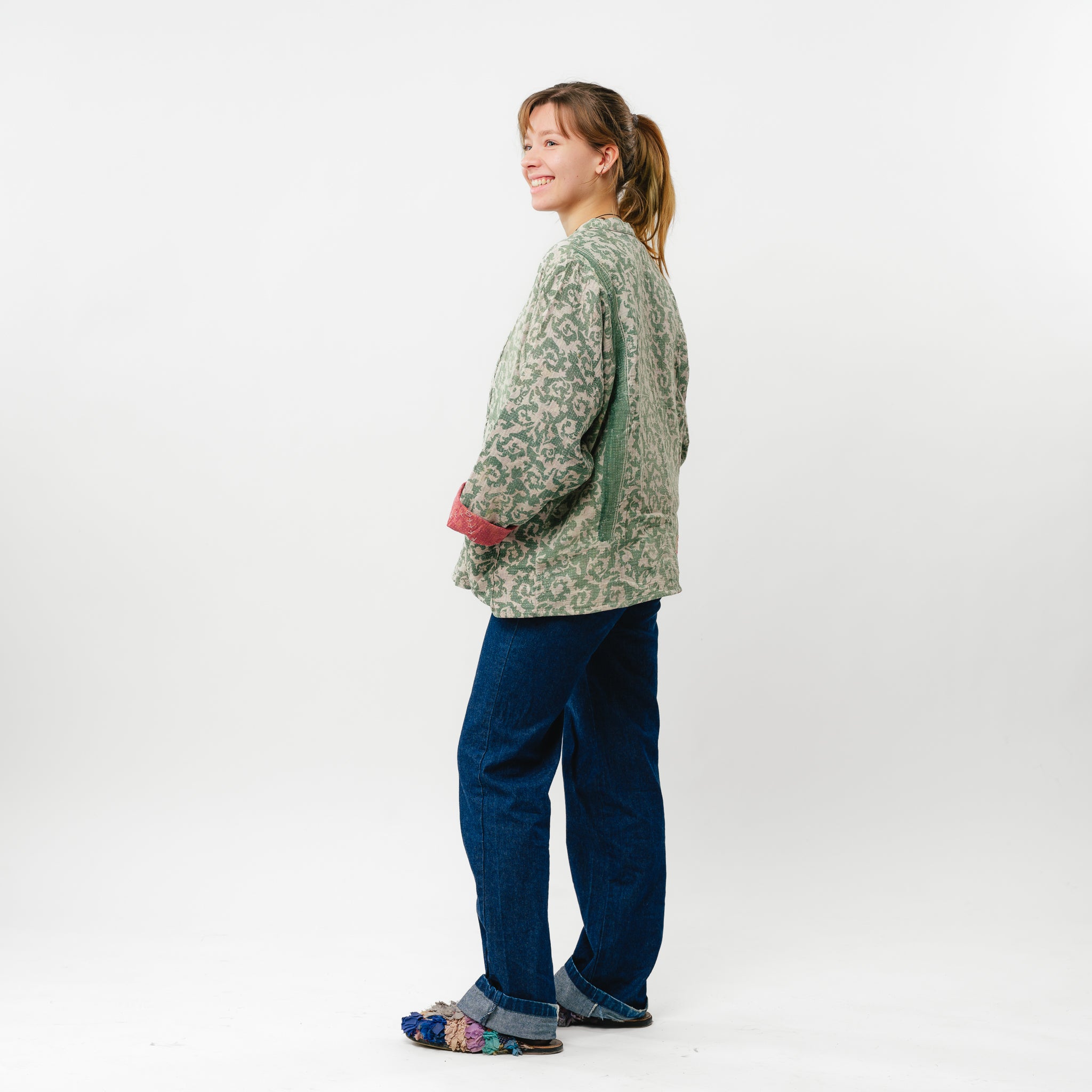 Person wearing a patterned cardigan and blue pants on a white background