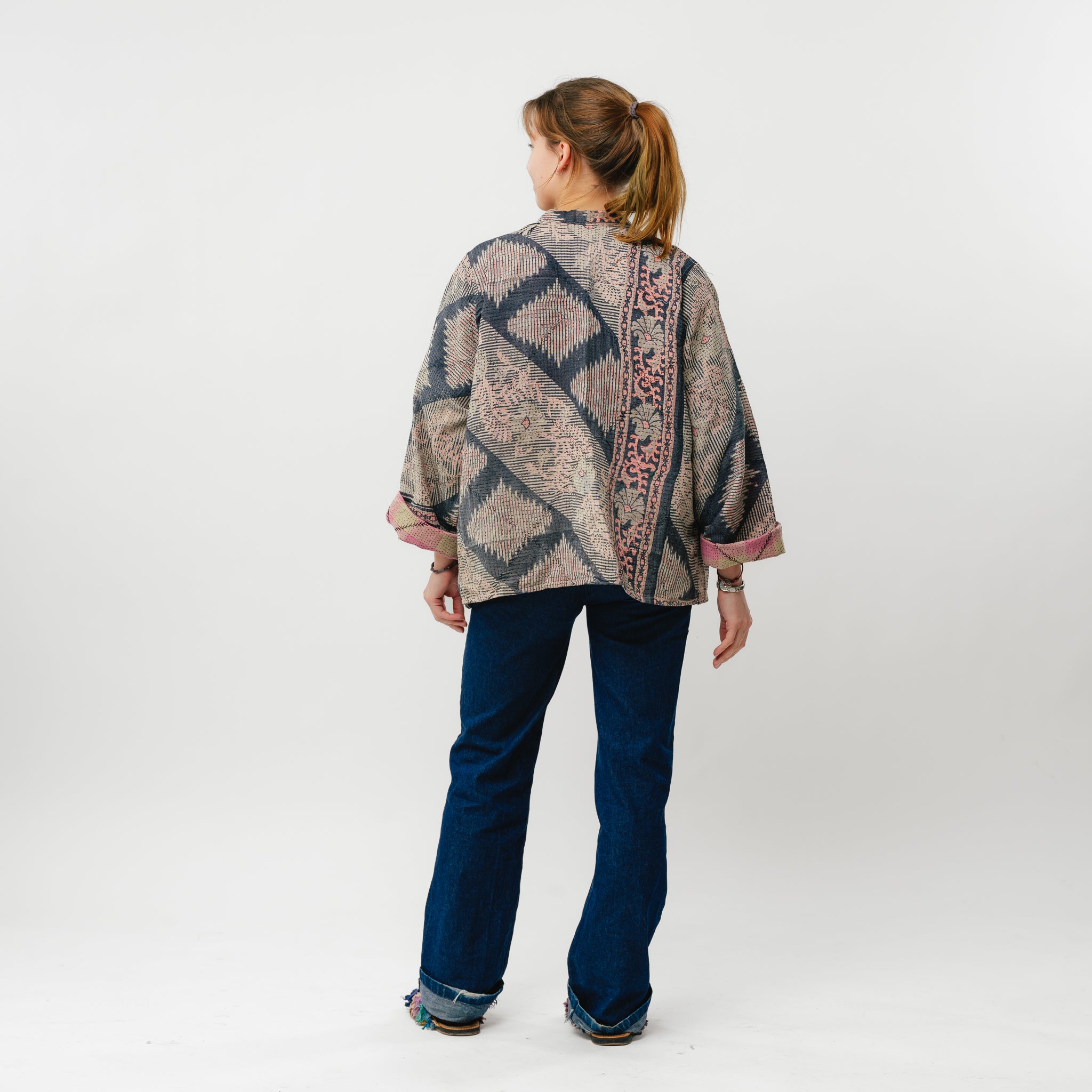 Woman wearing a patterned top and blue jeans on a white background