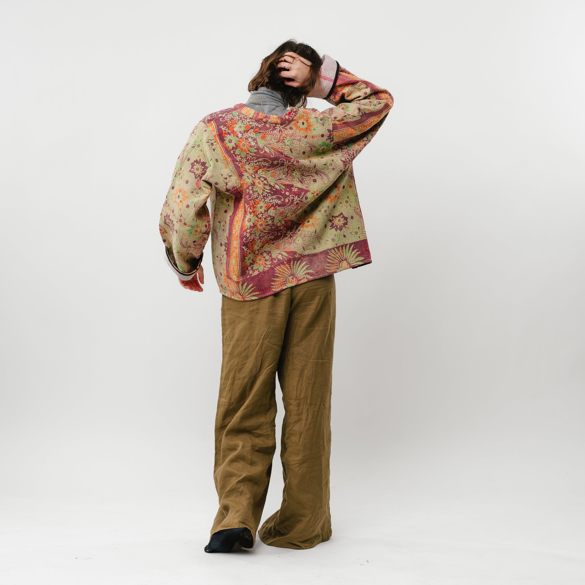 Person wearing a patterned sweater and brown pants on a white background