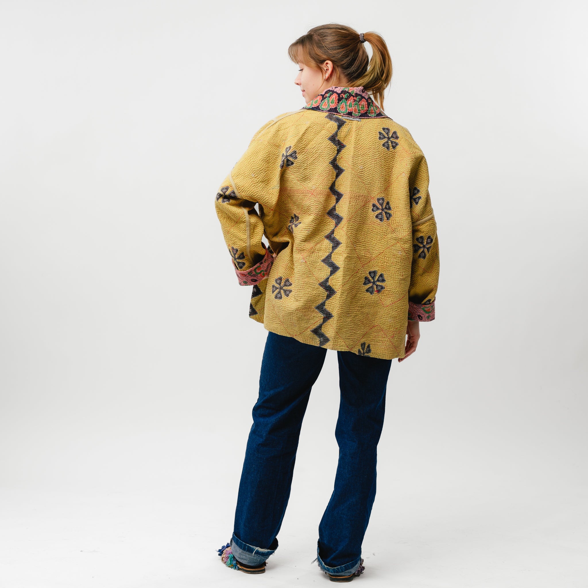 Person wearing a mustard yellow embroidered jacket on a white background