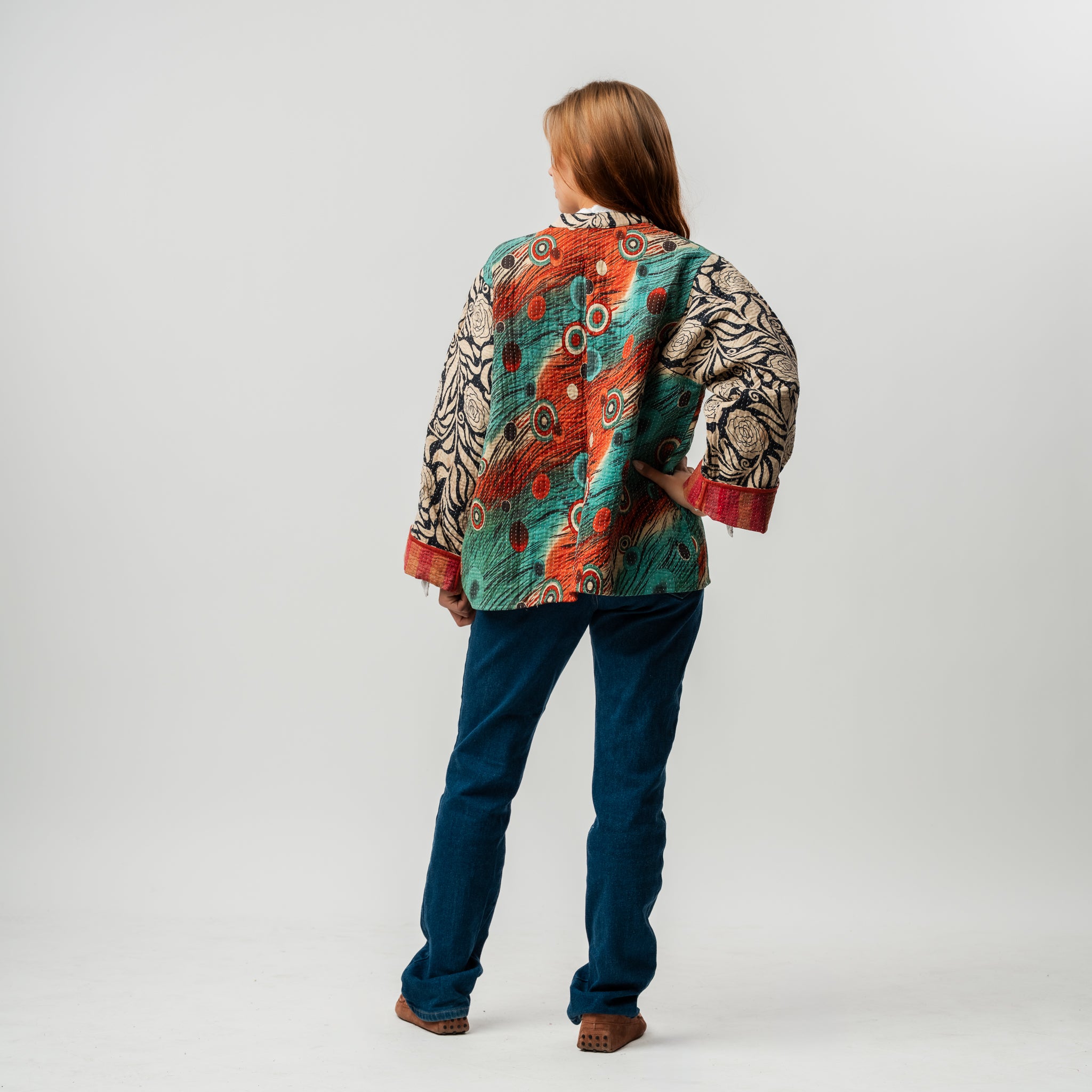 Person wearing a colorful patterned jacket and blue pants on a white background