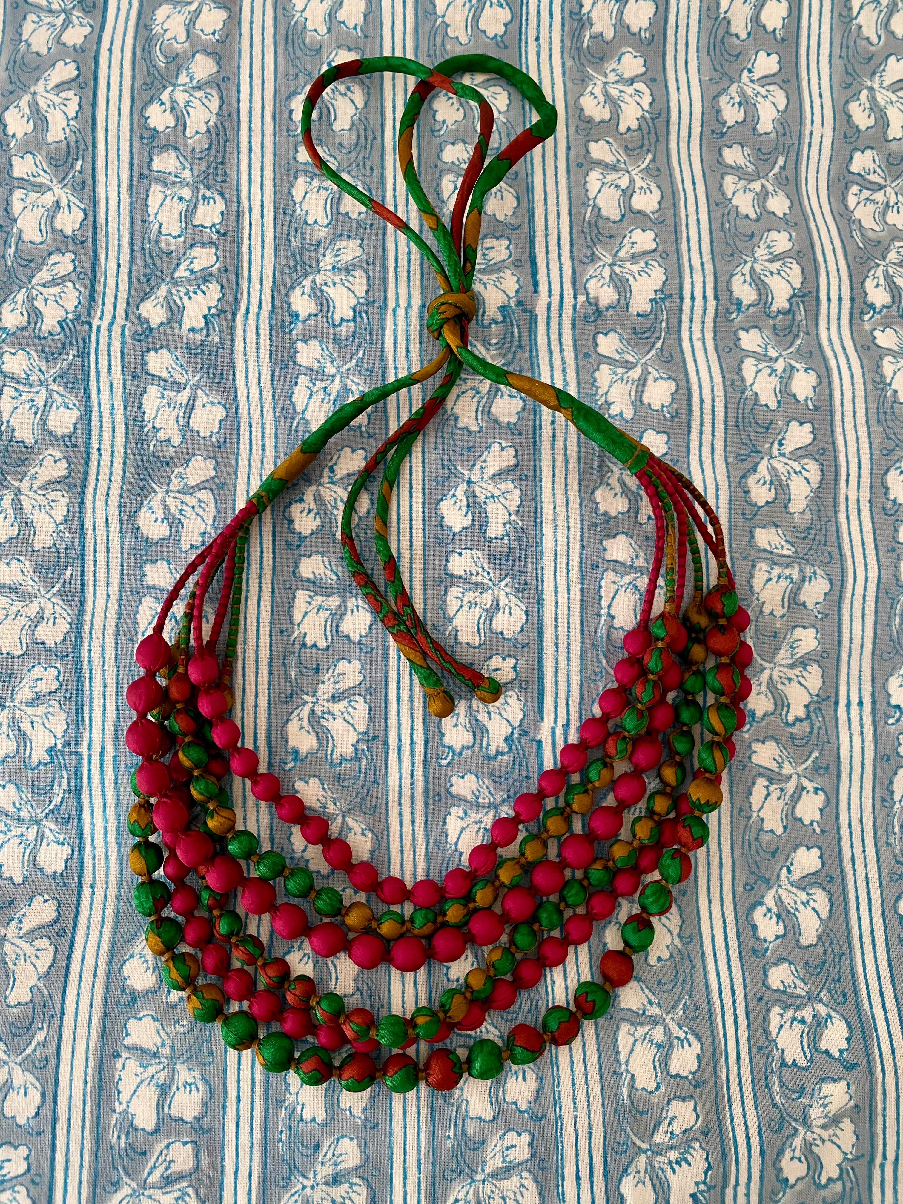 Colorful beaded necklace on a blue floral-patterned fabric background