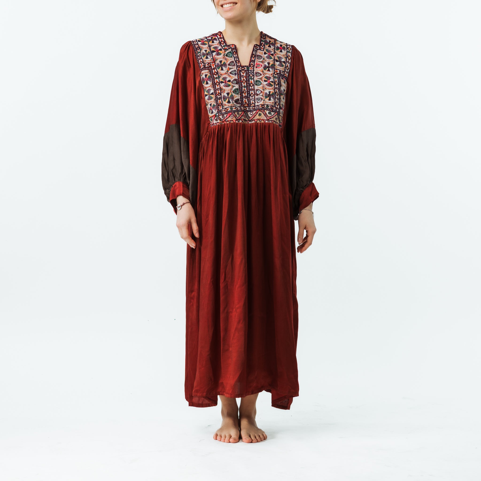 Person wearing a long burgundy dress with patterned top on a white background
