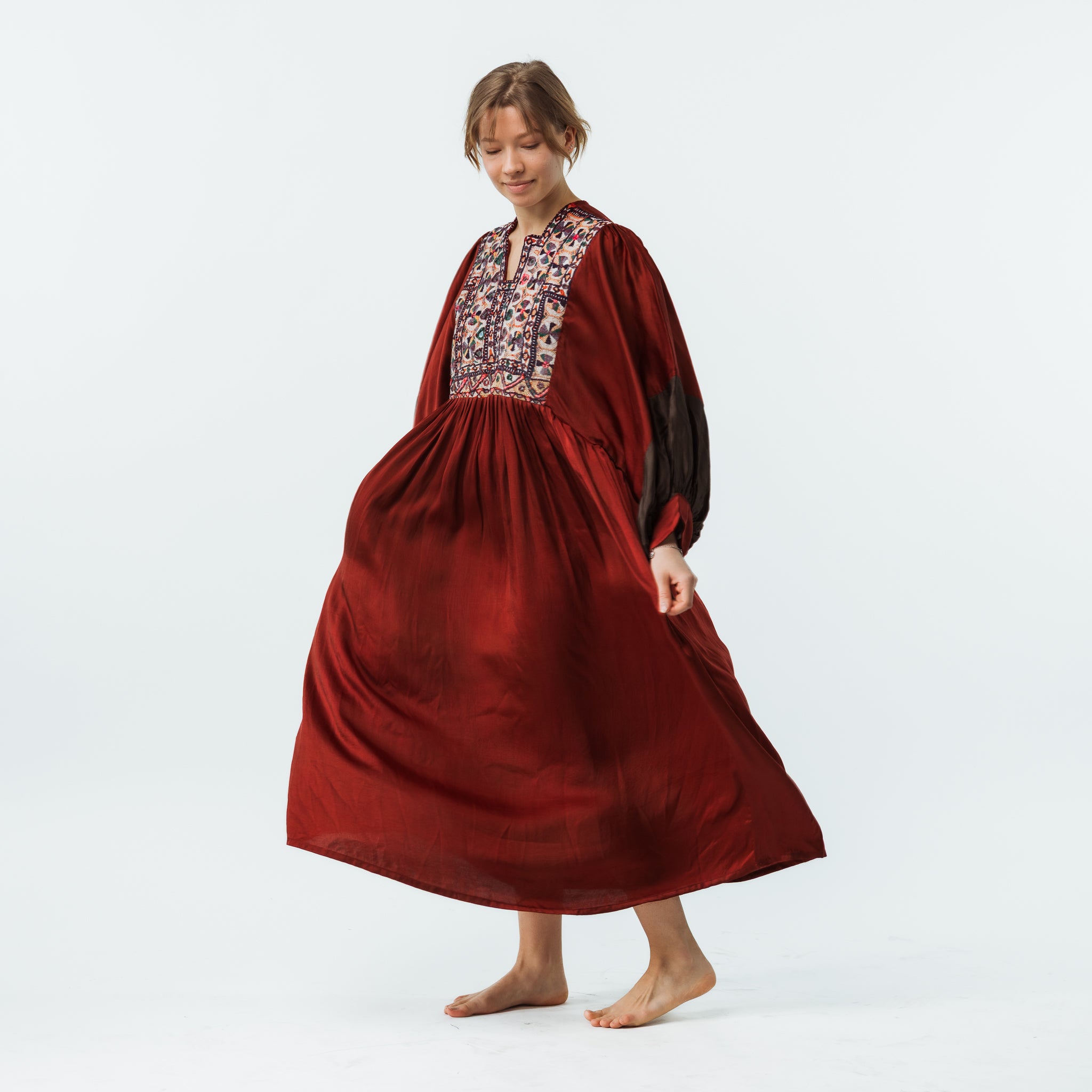 Woman wearing a long burgundy dress with floral embroidery on a white background