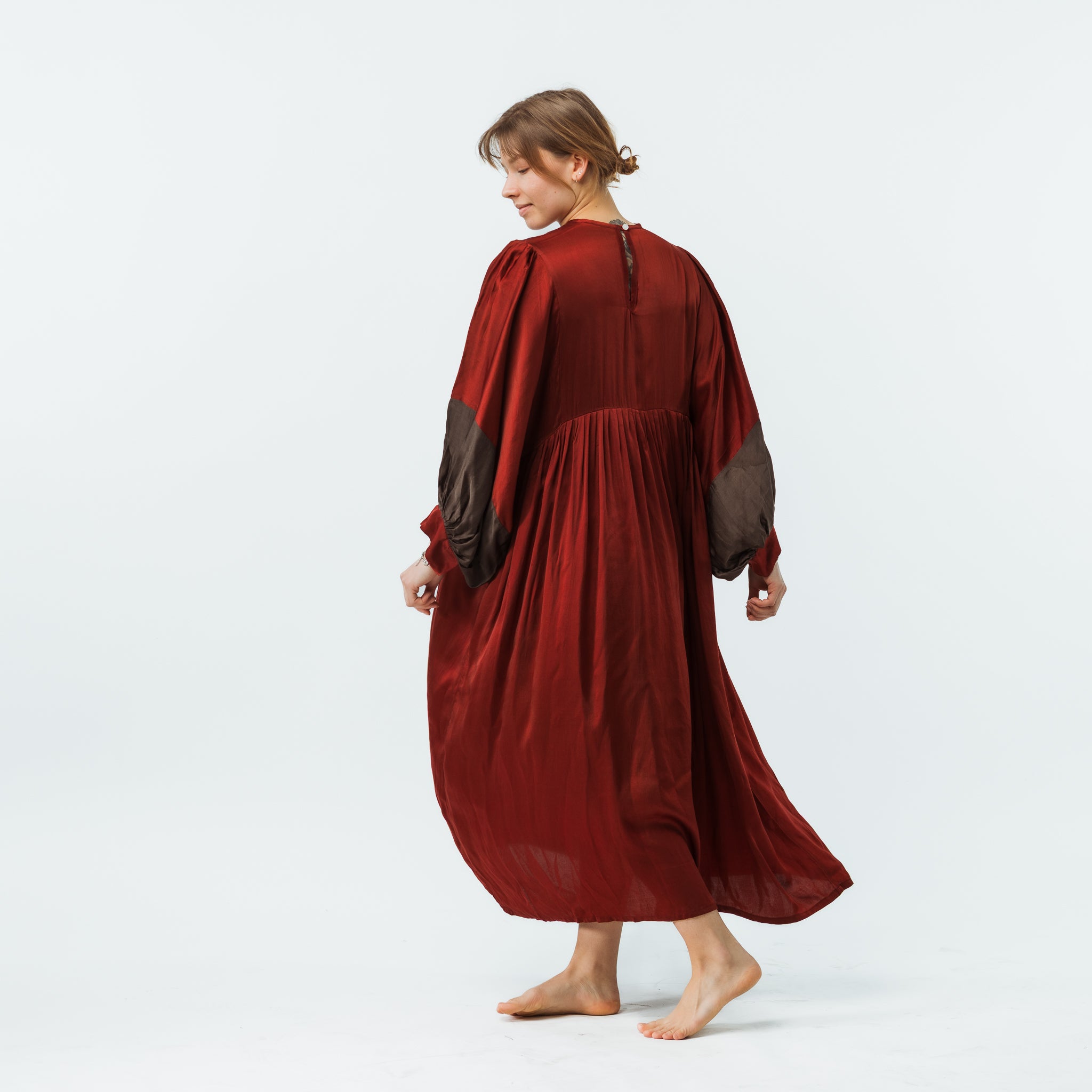 Woman wearing a long red dress with sheer sleeves on a white background