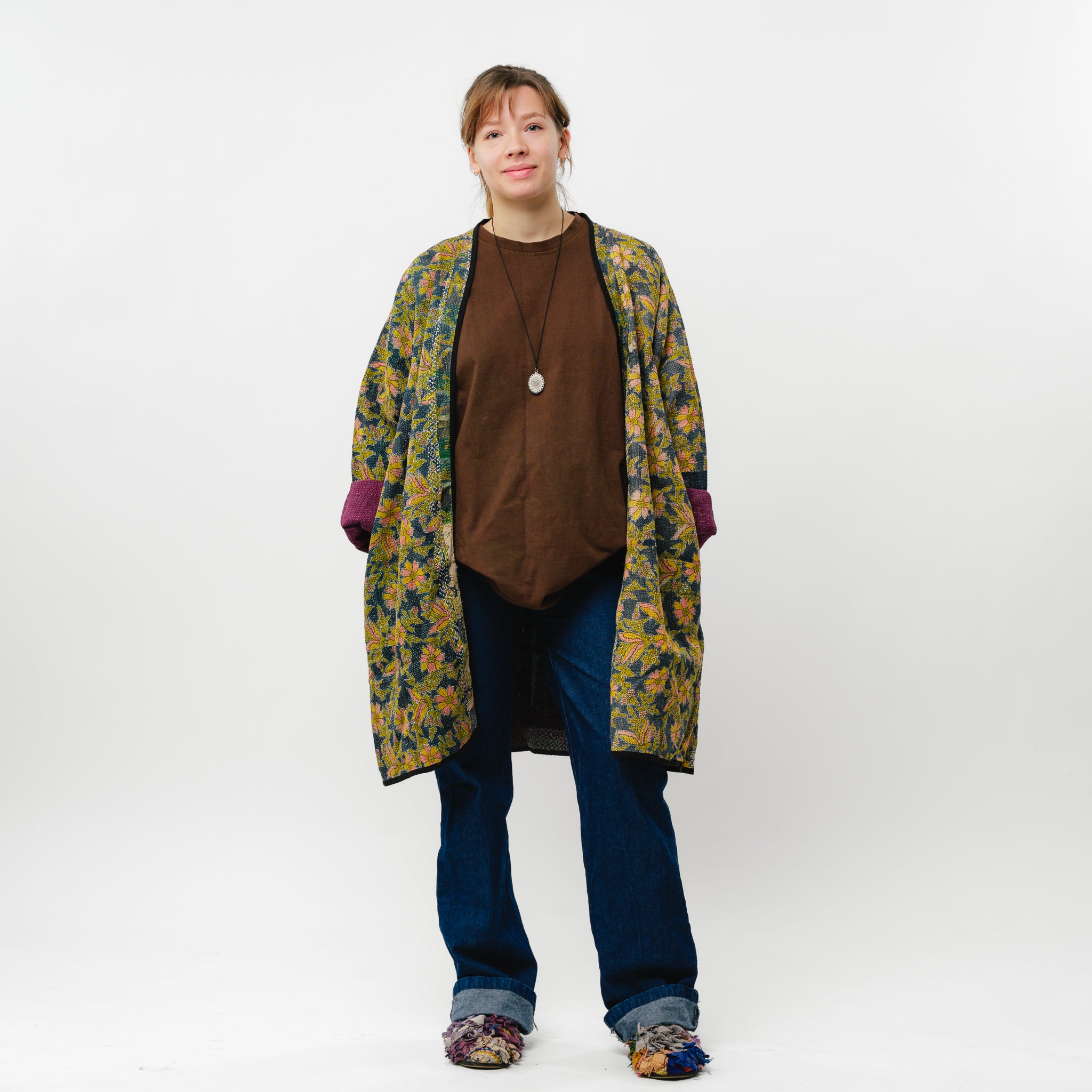 Person wearing a floral coat over a brown top and blue jeans on a white background