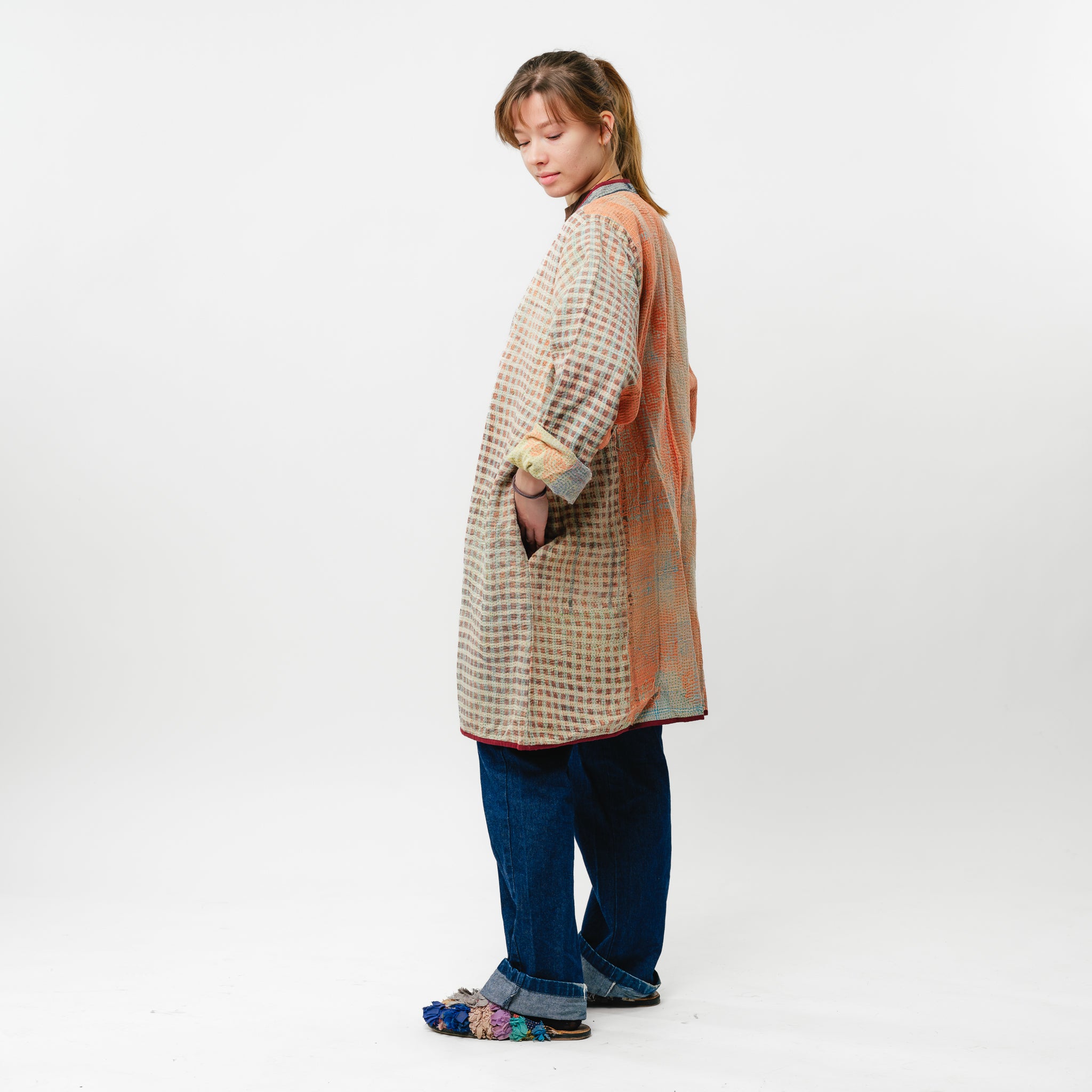 Person wearing a patterned coat and blue jeans on a white background