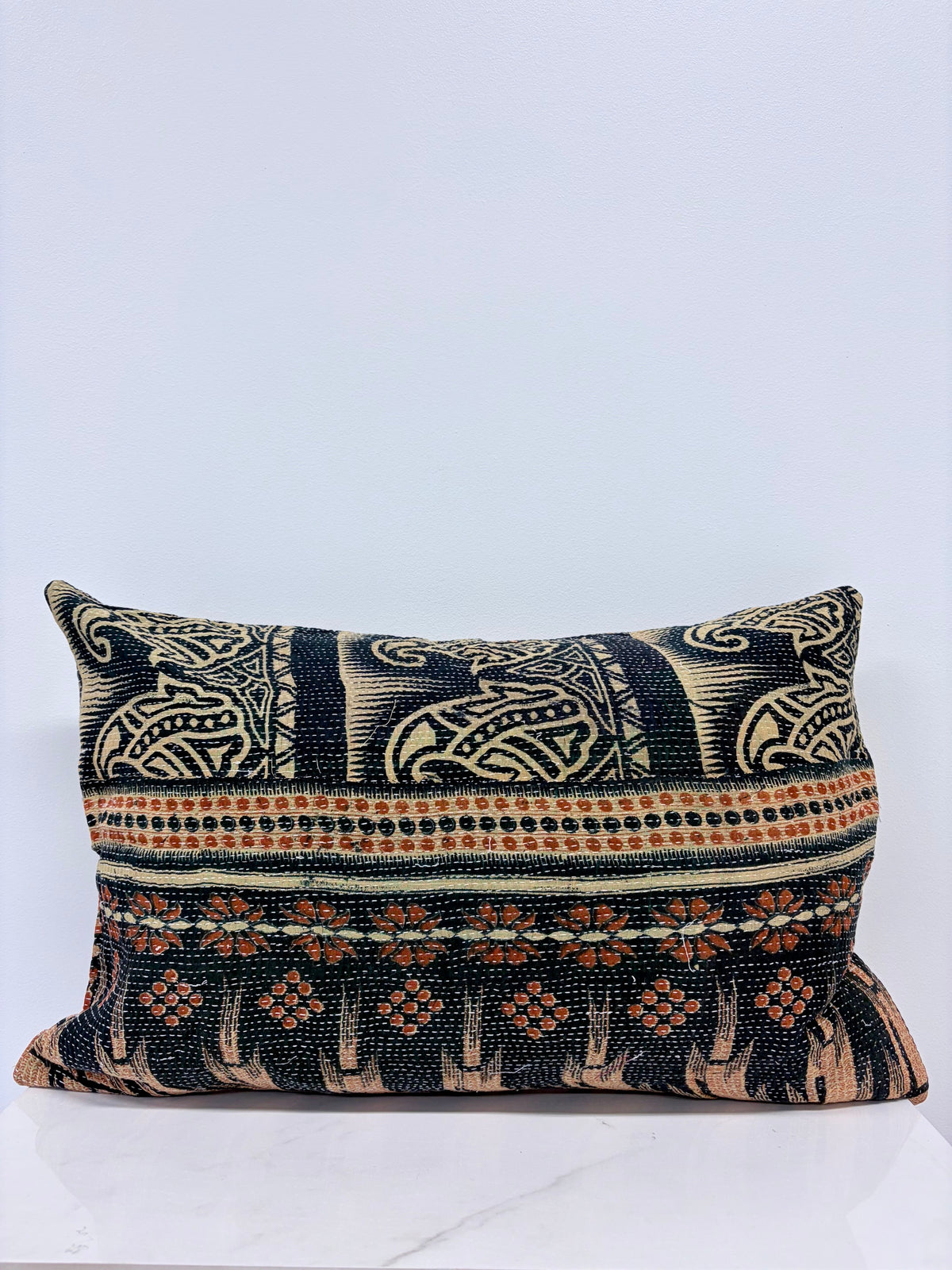 A square decorative throw pillow featuring a detailed woven pattern with black, beige, and rust-orange horizontal bands, displayed on a light gray background.