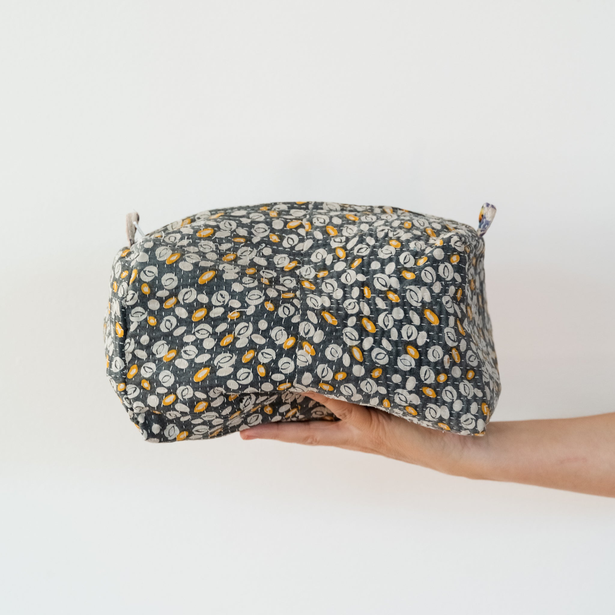 Hand holding a floral-patterned fabric pouch against a white background