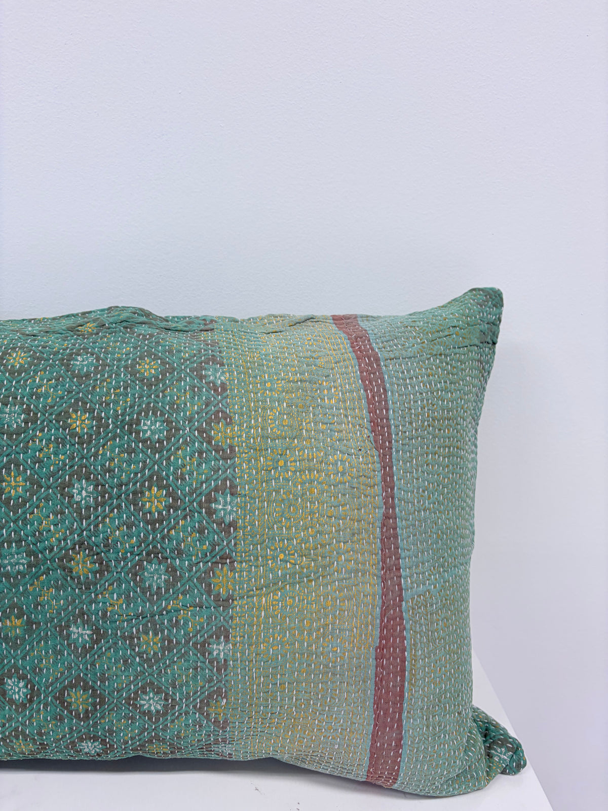 A square woven throw pillow in a muted teal green color, featuring a geometric pattern on one side, a vertical red stripe, and a yellow-green textured center panel.