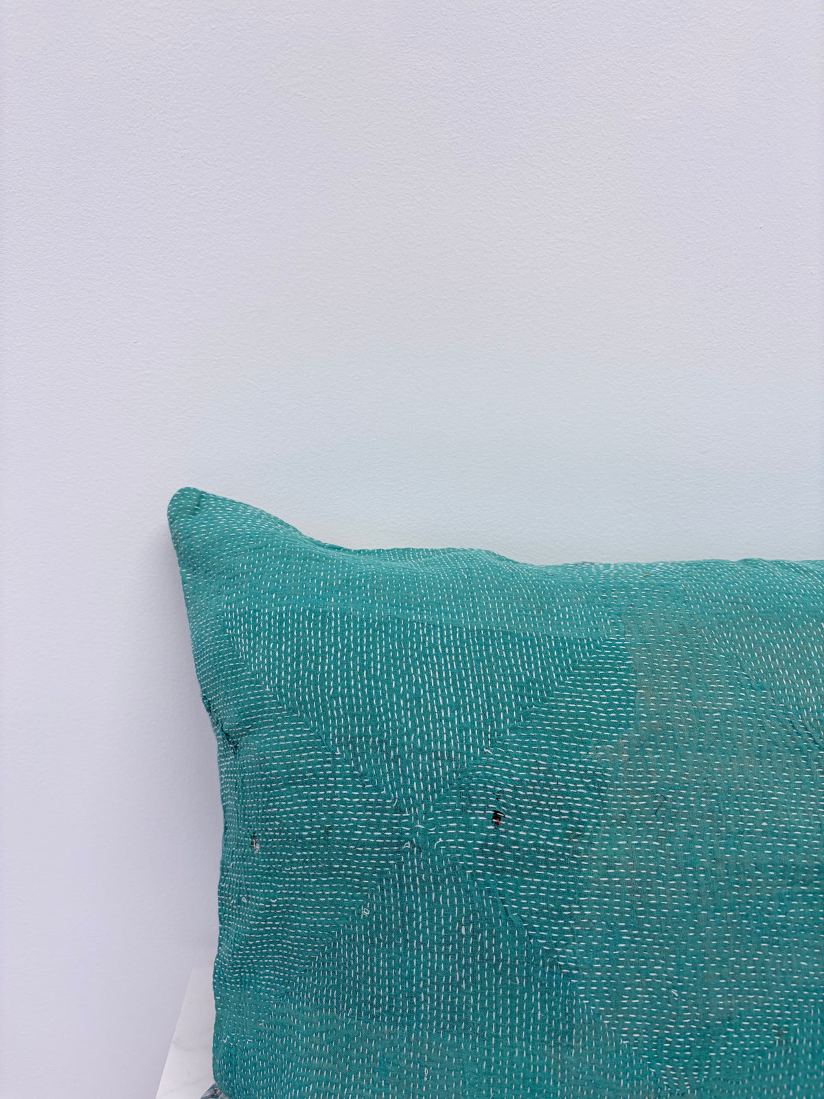 A close-up of a textured teal throw pillow corner against a plain white wall.
