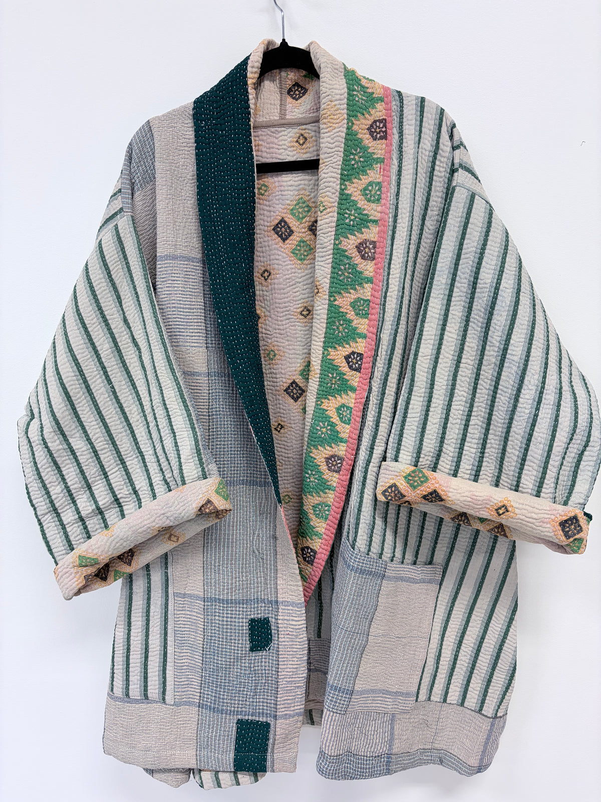 A patchwork-style kimono robe with vertical stripes, plaid panels, and decorative patterned trim, hanging on a black hanger against a plain white background.