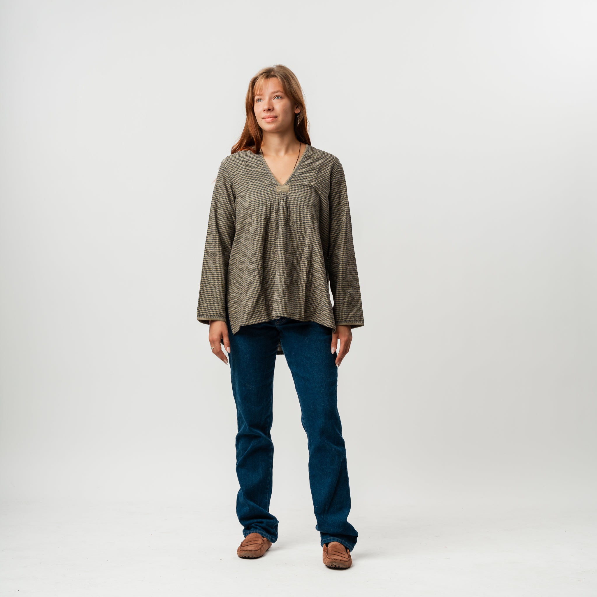 Woman wearing a green patterned top and blue jeans on a white background