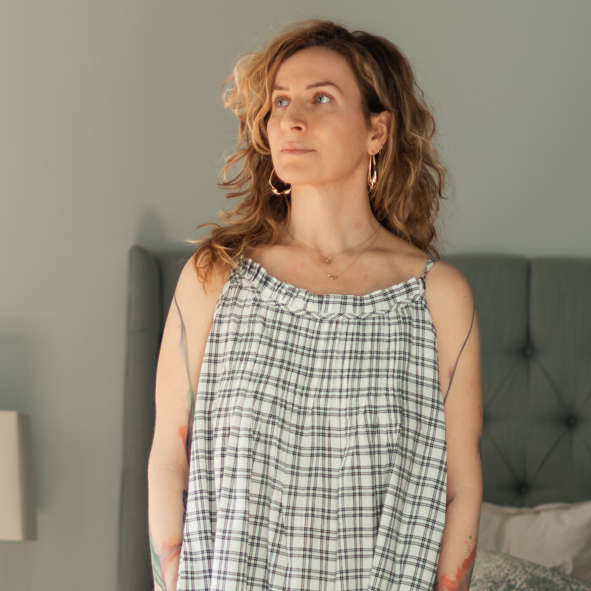 Woman wearing a plaid dress standing in a bedroom.