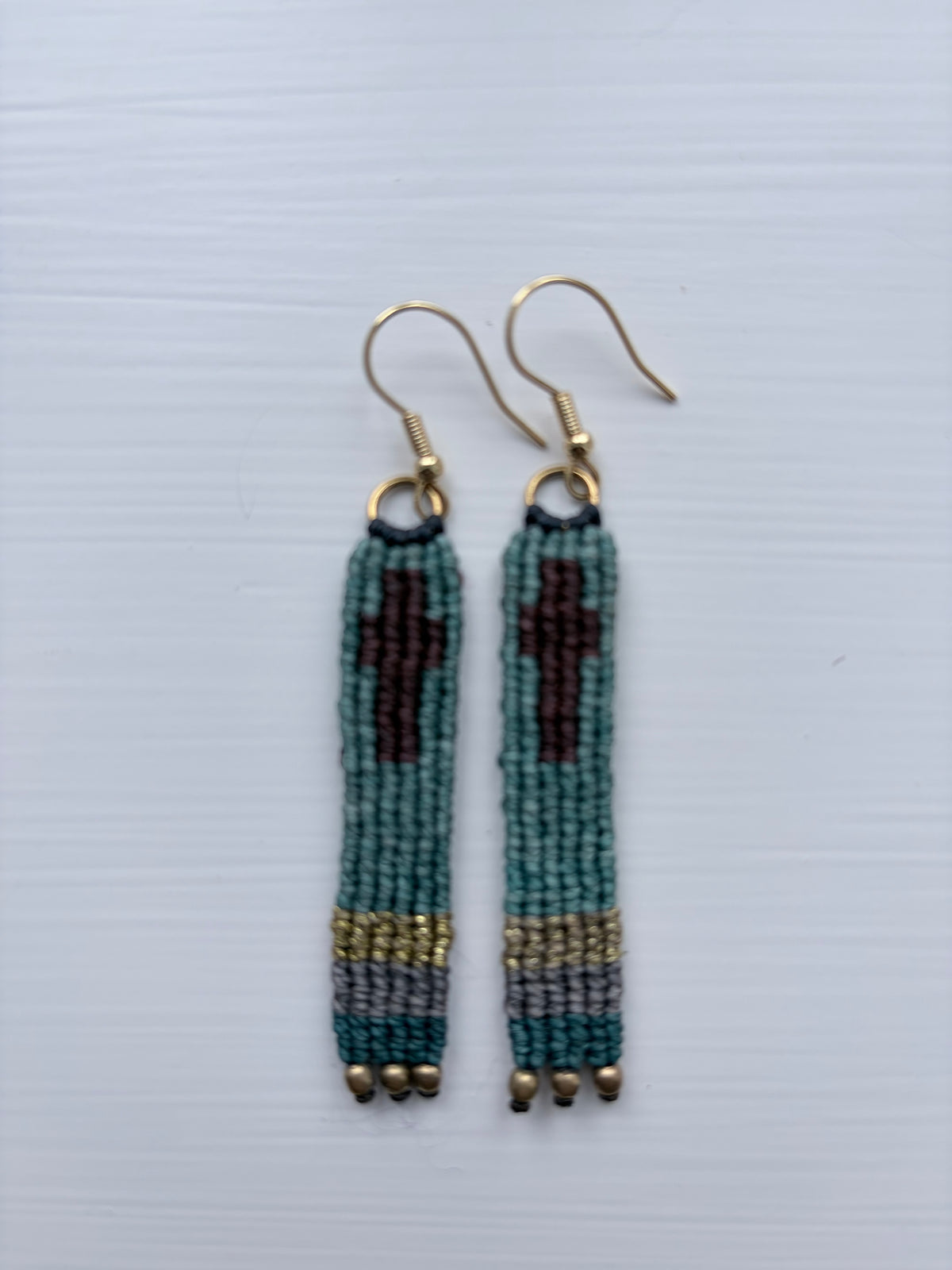 A pair of handmade beaded dangle earrings with gold fishhook wires. The beads are primarily teal green with a dark red geometric motif in the center, a gray and gold striped section near the bottom, and small gold beads hanging from the ends.