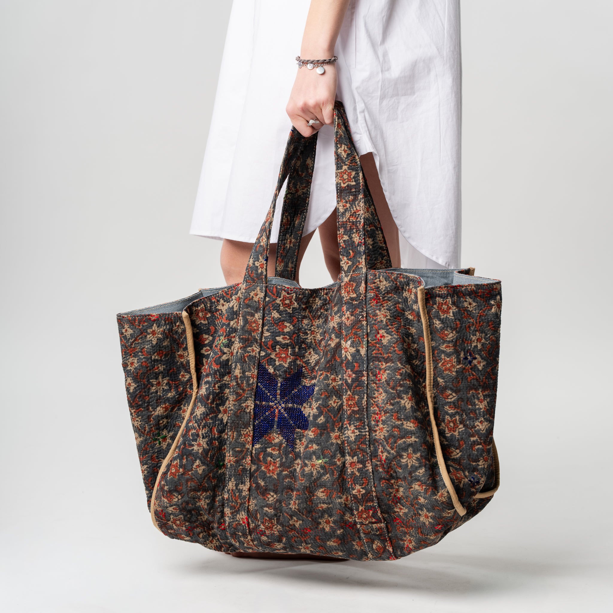 Floral-patterned tote bag held by a person wearing a white outfit on a light gray background