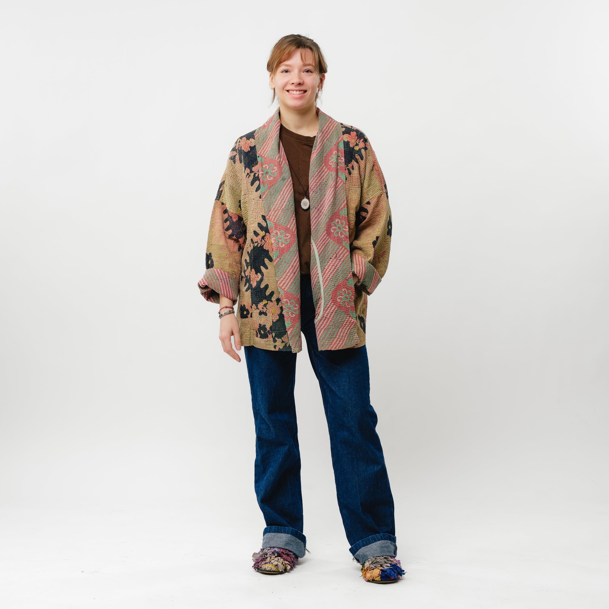 Person wearing a patterned coat and jeans on a white background