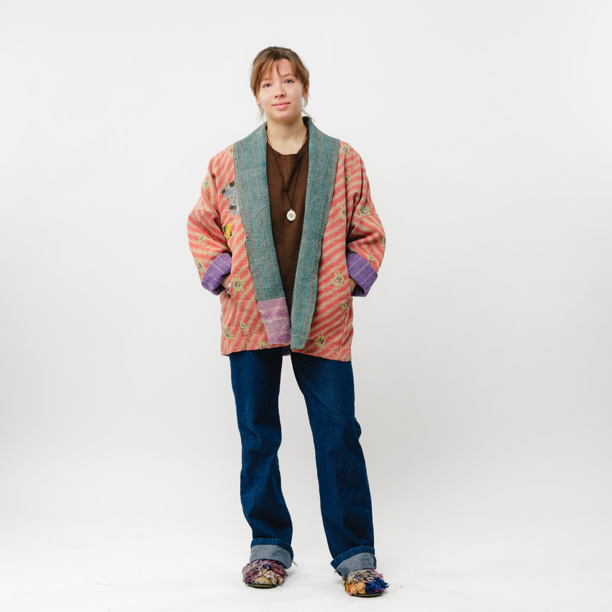 Person wearing a colorful cardigan and blue jeans on a white background