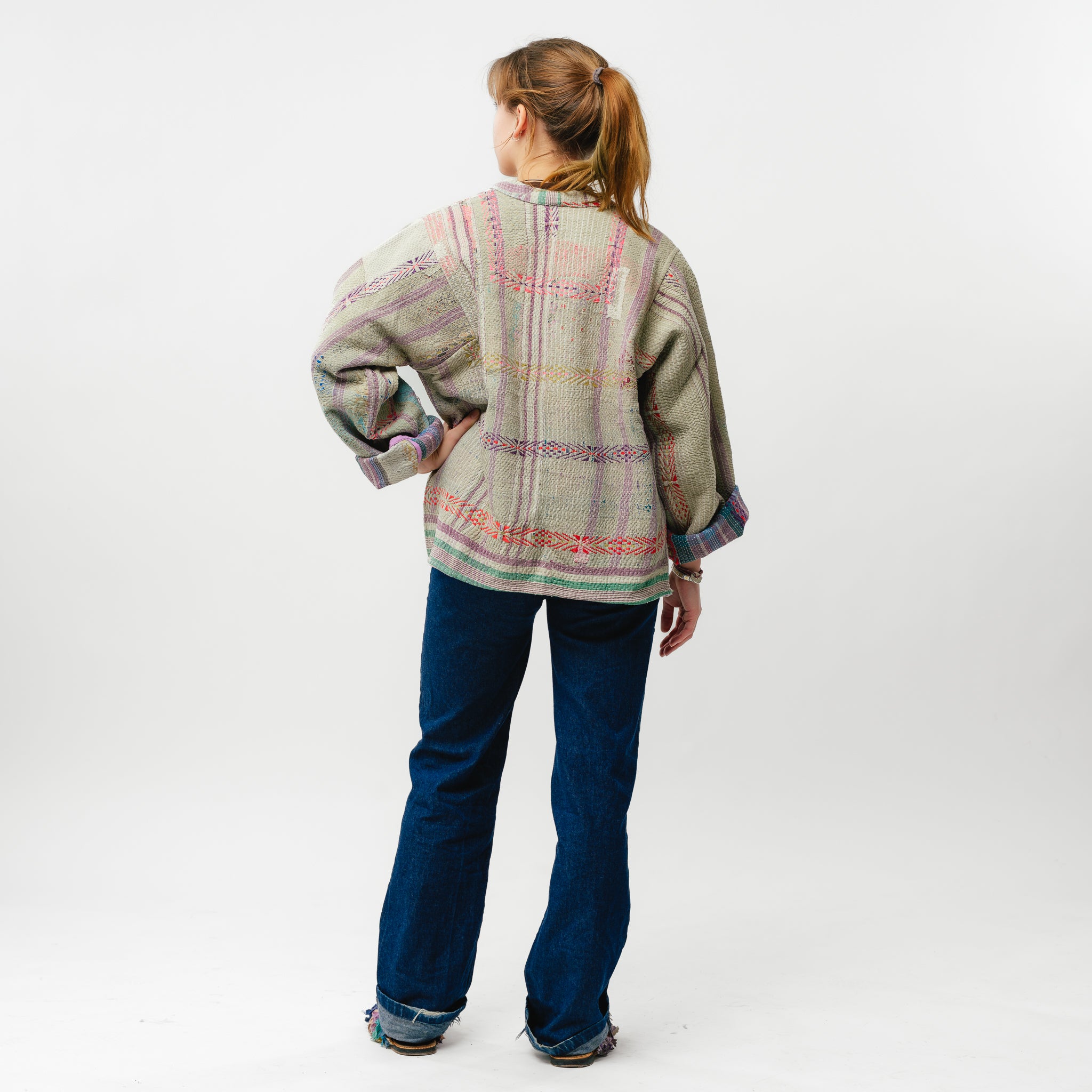 Person wearing a patterned jacket and blue jeans on a white background