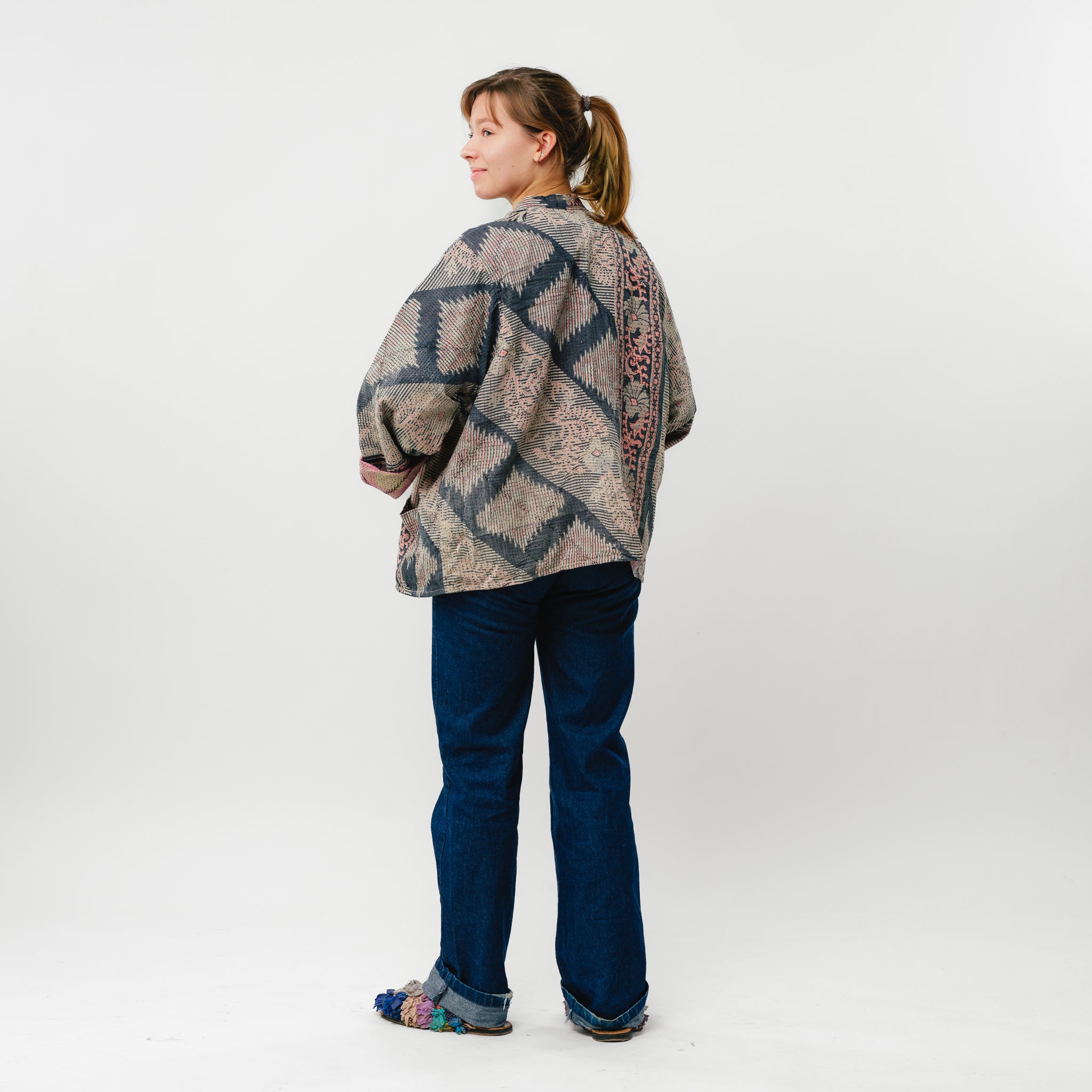 Person wearing a patterned jacket and blue jeans on a white background