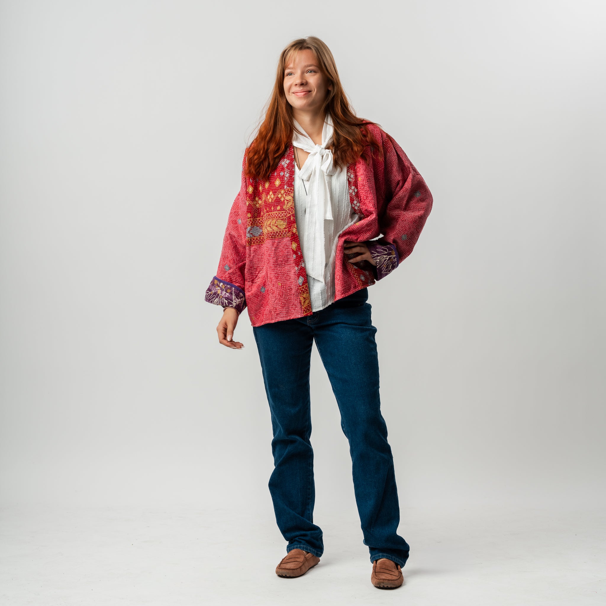 Woman wearing a red patterned jacket over a white shirt and blue jeans on a light gray background