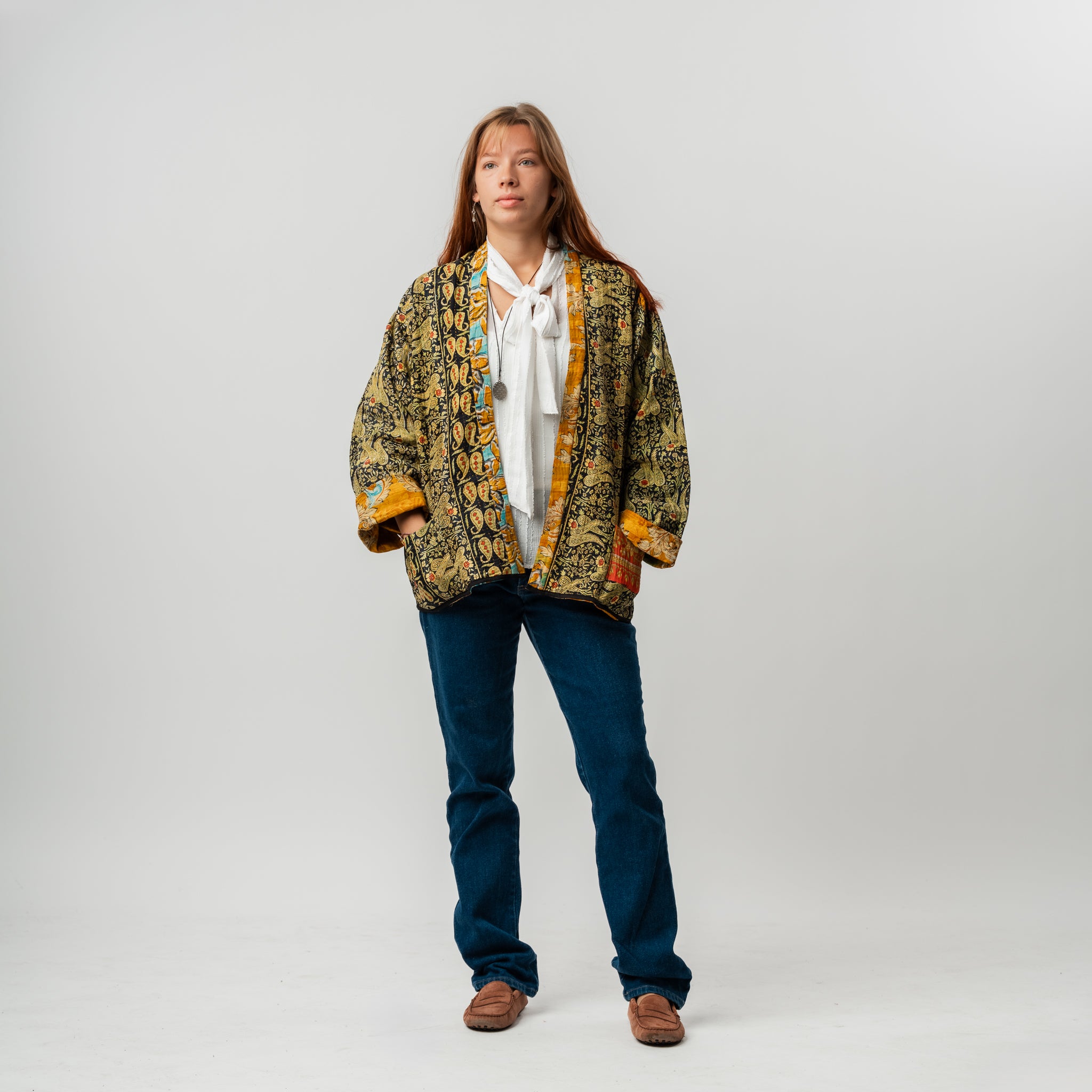 Person wearing a patterned jacket and blue jeans on a plain background