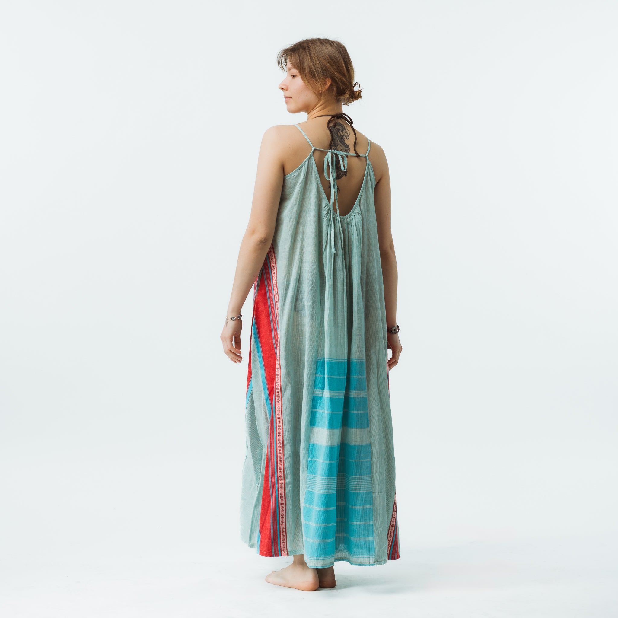 Woman wearing a long, light green dress with colorful side panels on a white background