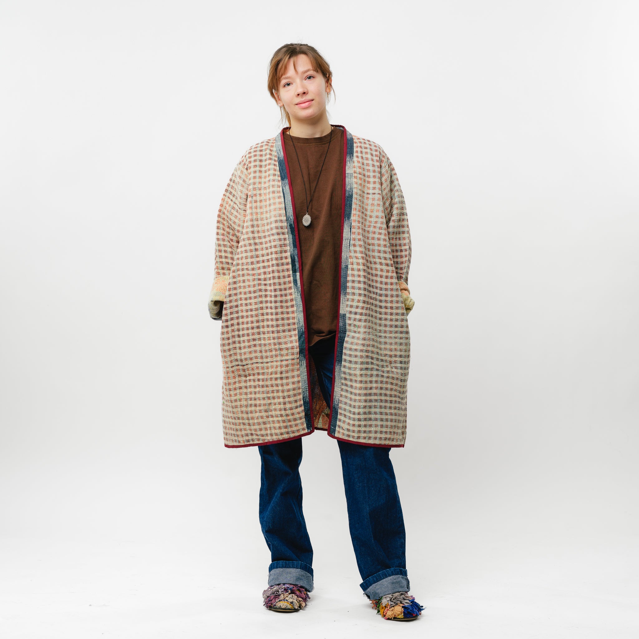 Person wearing a long plaid coat over a brown shirt on a white background