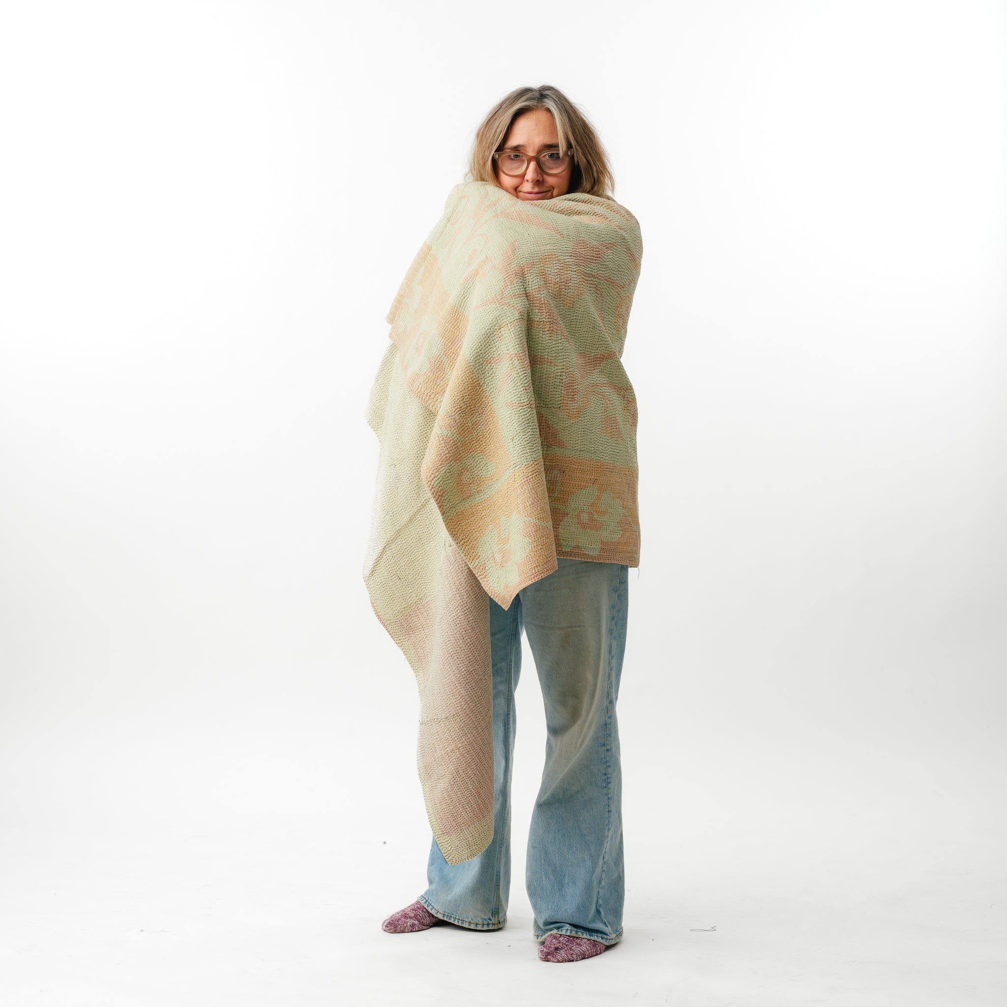 Woman wrapped in a large beige blanket with a subtle pattern on a white background