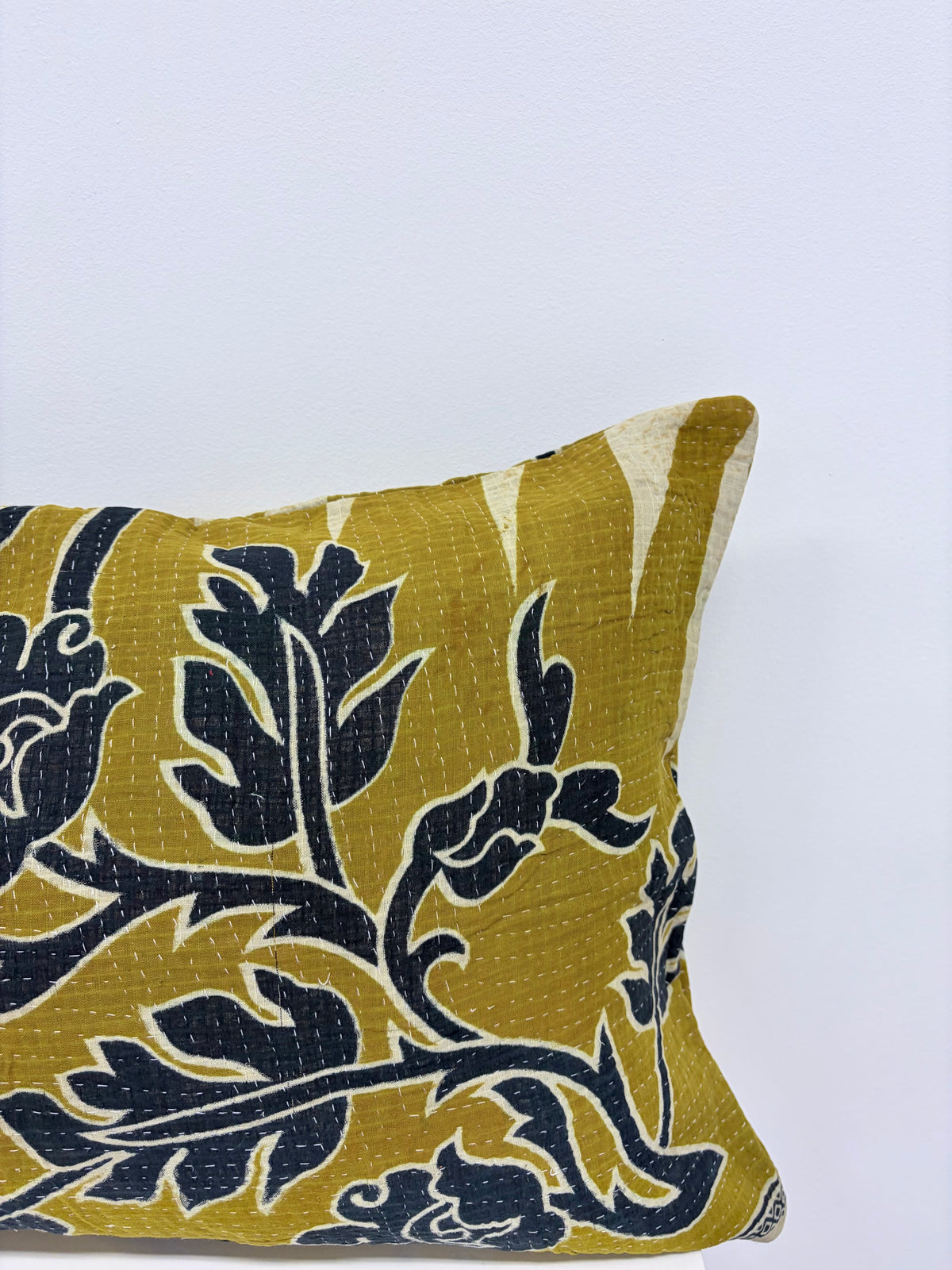 A close-up of a decorative throw pillow featuring a mustard yellow and navy blue floral block-print pattern on a light gray background.
