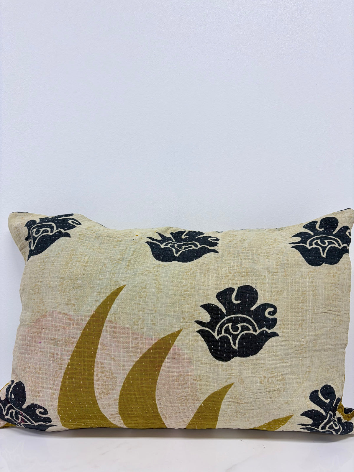 A square decorative throw pillow with a textured cream linen-like fabric, featuring black floral motifs and mustard yellow and pale pink abstract leaf shapes.