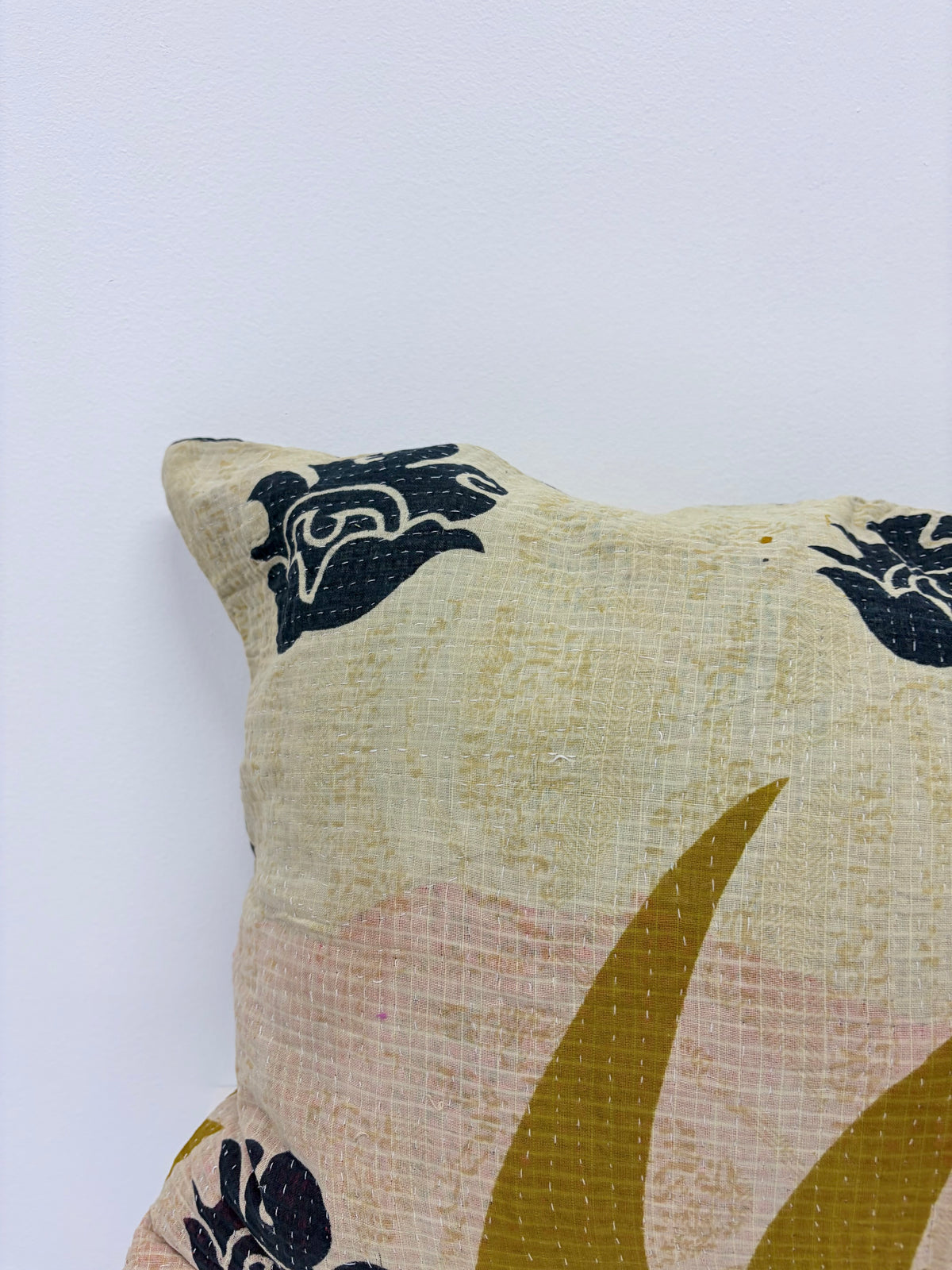 A close-up of a textured throw pillow featuring a hand-block printed floral pattern in black, mustard yellow, and soft pink on a cream-colored fabric, set against a plain white background.