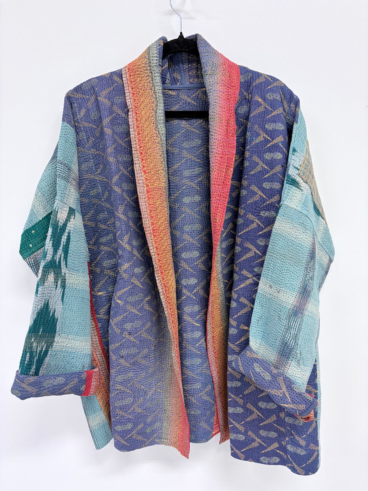 A lightweight open-front kimono-style cardigan with a blue-purple base, woven geometric patterns, and striped panels in teal, pink, orange, and cream, hanging on a black hanger against a white background.