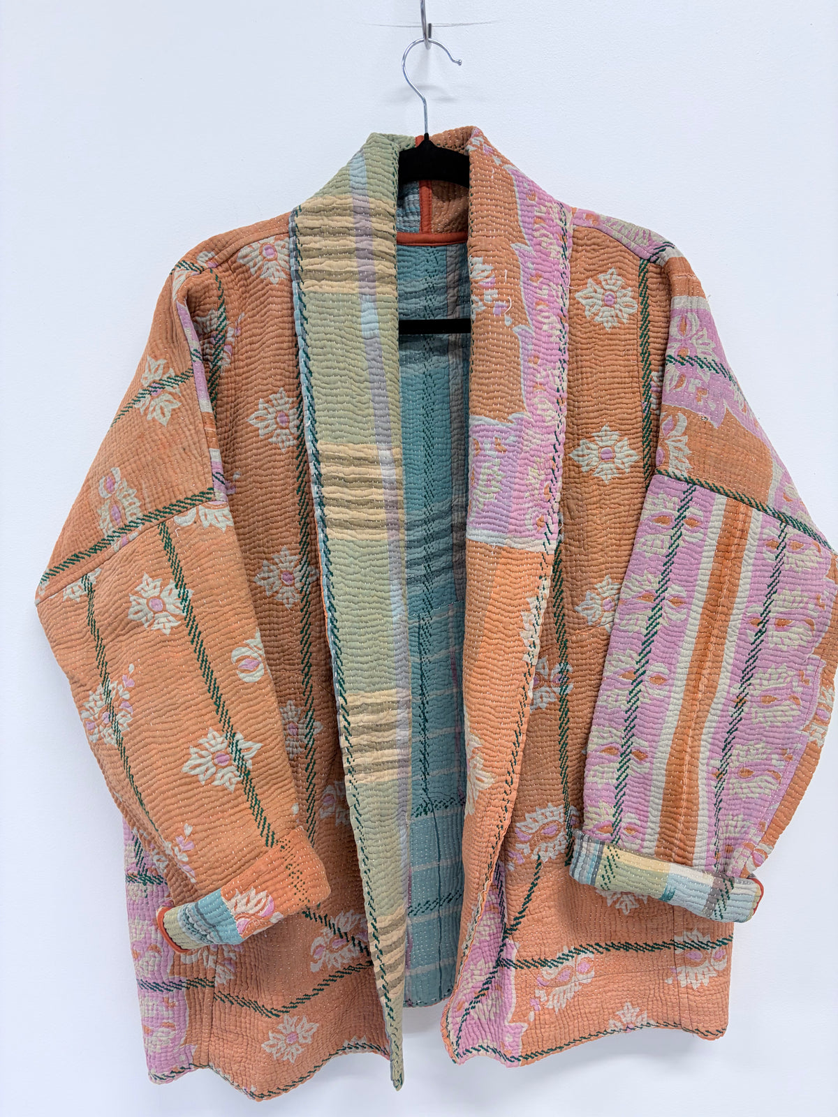 A lightweight patchwork kimono-style cardigan jacket with a shawl collar, featuring a mix of peach, pink, green, and blue patterned fabrics, hanging on a black hanger against a plain white background.