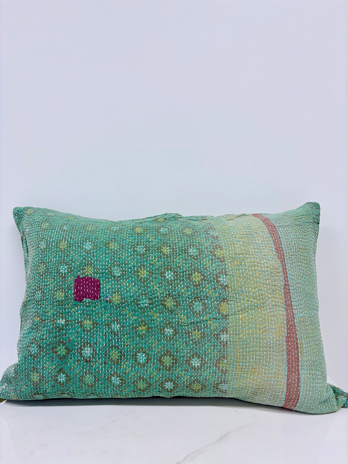 A rectangular lumbar throw pillow made from a vintage green and yellow patterned silk fabric, featuring a small magenta embroidered patch on the left and a vertical dusty pink stripe on the right.