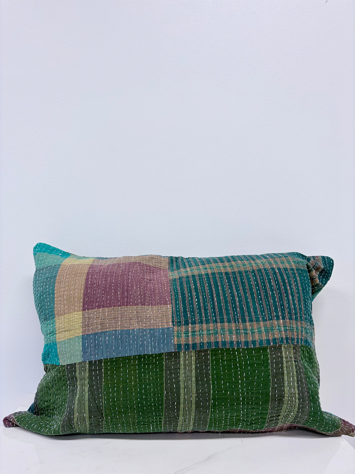 A square patchwork kantha pillow made from multiple green, teal, purple, and beige woven fabrics, displayed against a plain white background.