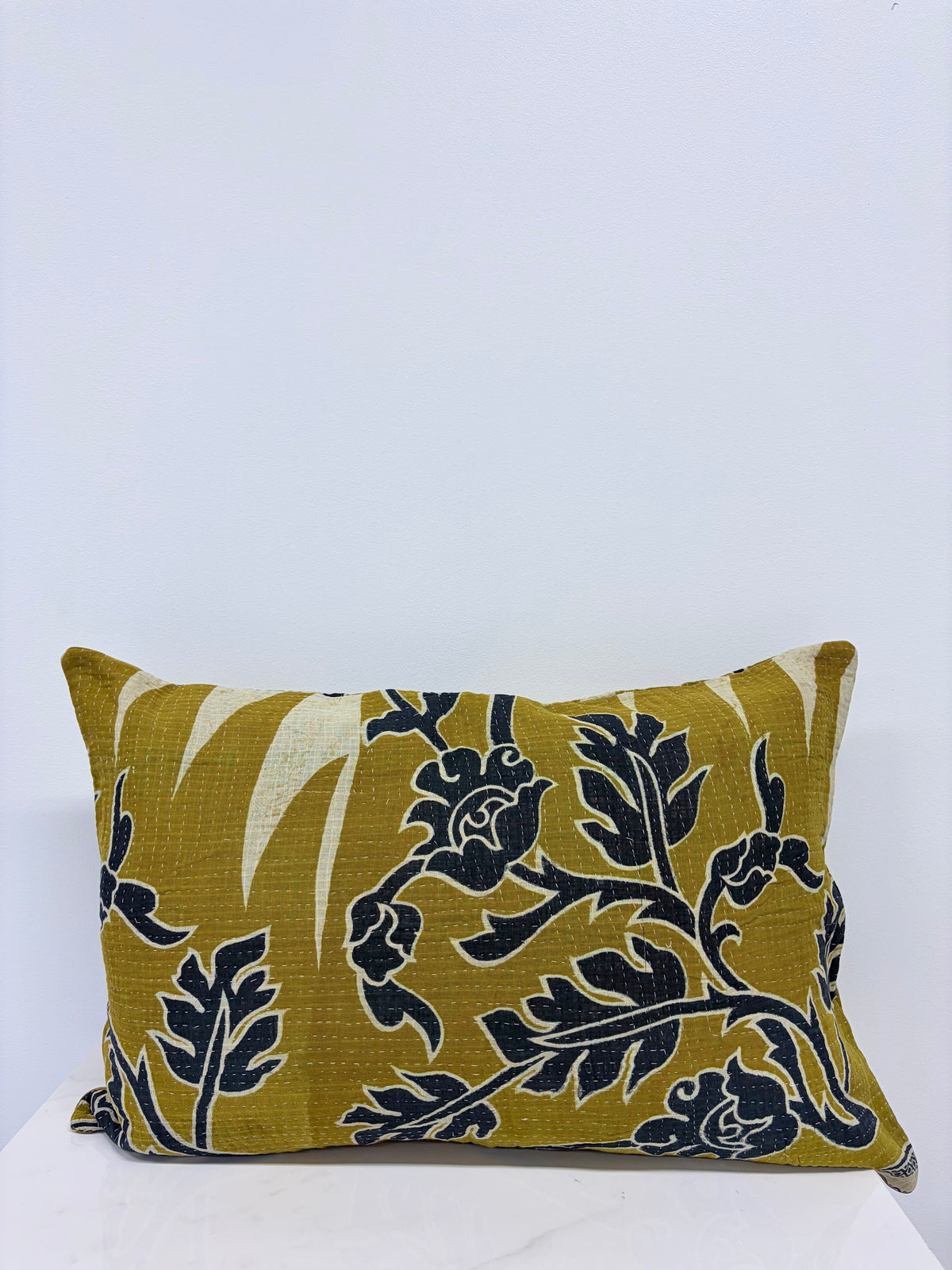 A rectangular decorative throw pillow with a mustard yellow and black floral pattern, resting on a white surface against a plain white background.